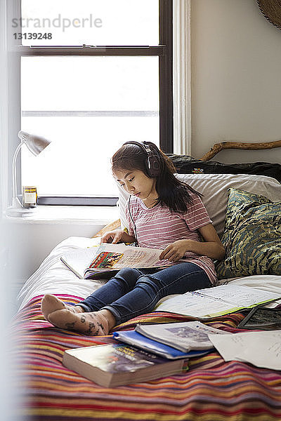 Teenagerin beim Lernen mit Kopfhörern am Bett zu Hause