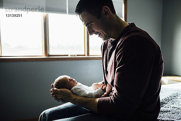 Glücklicher Vater trägt schlafende Tochter  während er zu Hause auf dem Bett sitzt