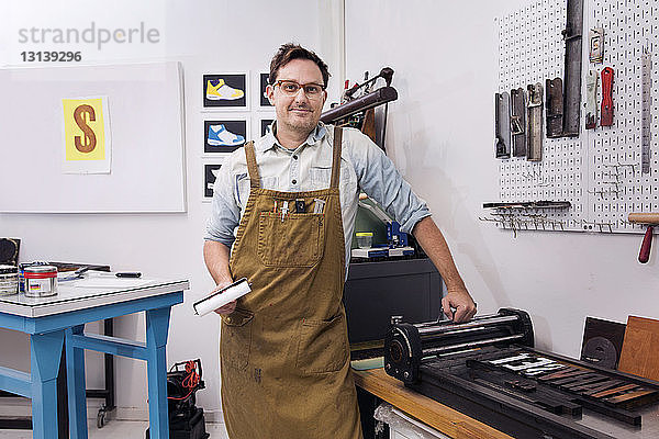 Lächelnder Arbeiter  der die Farbwalze hält  während er in der Druckmaschine steht