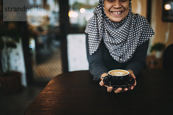 Lächelnde Frau in der Mitte  die Kaffee hält  während sie im Café sitzt