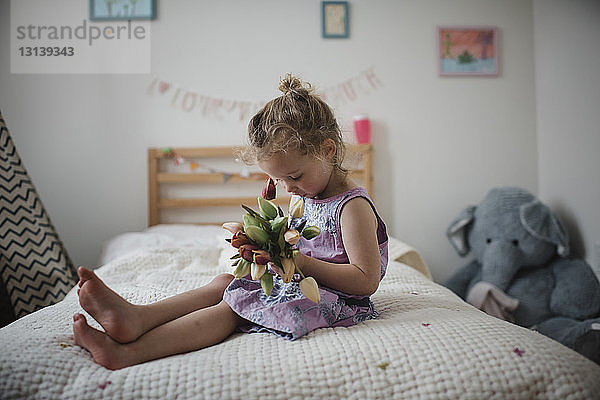 Mädchen hält Tulpen  während sie zu Hause auf dem Bett sitzt