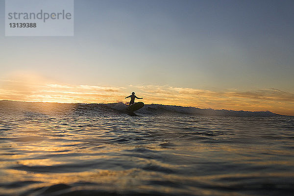 Fernansicht der Silhouette einer Frau  die bei Sonnenuntergang auf dem Meer surft