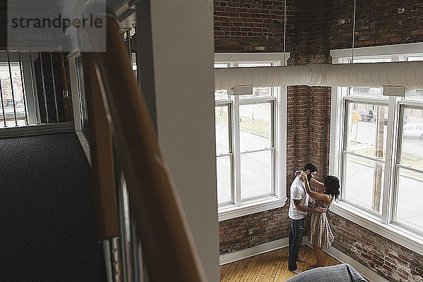 Hochwinkelansicht eines romantischen Paares  das sich umarmt  während es zu Hause an den Fenstern steht