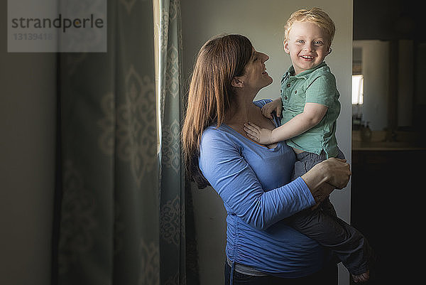 Porträt eines fröhlichen Sohnes  der von der Mutter zu Hause getragen wird