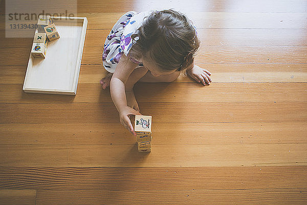 Hochwinkelaufnahme eines Mädchens  das zu Hause auf dem Boden sitzend mit Spielzeugklötzen spielt