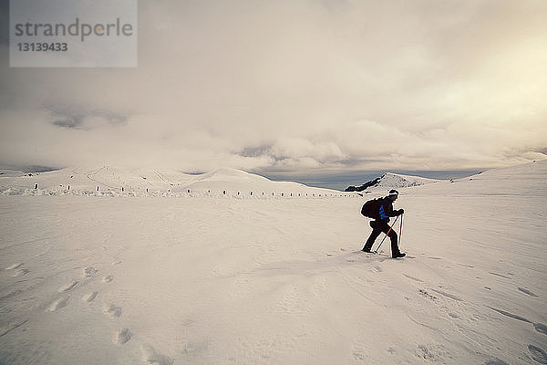 Seitenansicht eines Skifahrers  der auf Schnee vor bewölktem Himmel läuft