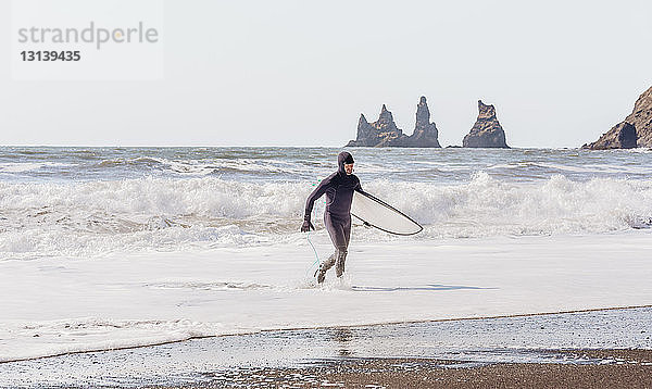 Mann mit Surfbrett geht am Strand bei klarem Himmel am sonnigen Tag