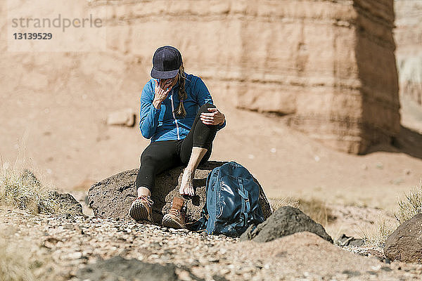 Müde Wanderin mit Rucksack entspannt sich am sonnigen Tag auf einem Felsen in der Wüste