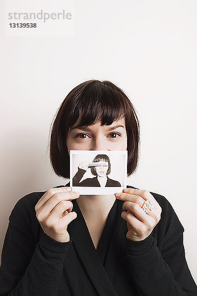 Porträt einer Frau  die ihr Foto zeigt  während sie an der Wand steht