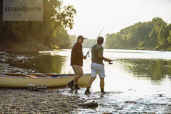 Männliche Freunde halten Angelruten in der Hand und unterhalten sich beim Spaziergang am Seeufer
