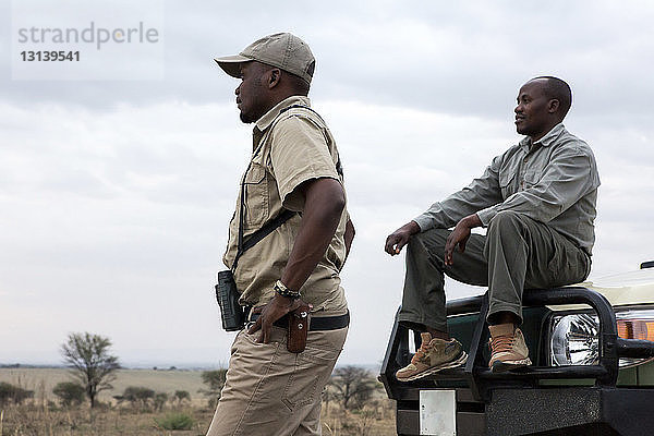 Männliche Freunde mit Geländewagen gegen bewölkten Himmel im Serengeti-Nationalpark