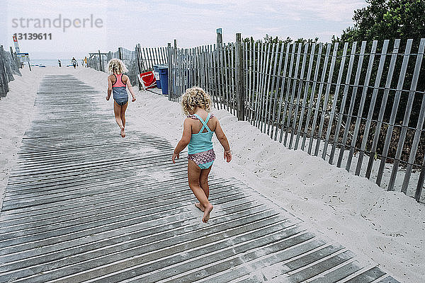 Rückansicht von Schwestern in Badebekleidung beim Spaziergang an der Strandpromenade