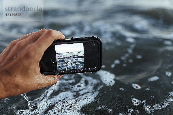Ausgeschnittene Hand beim Fotografieren des Meeres
