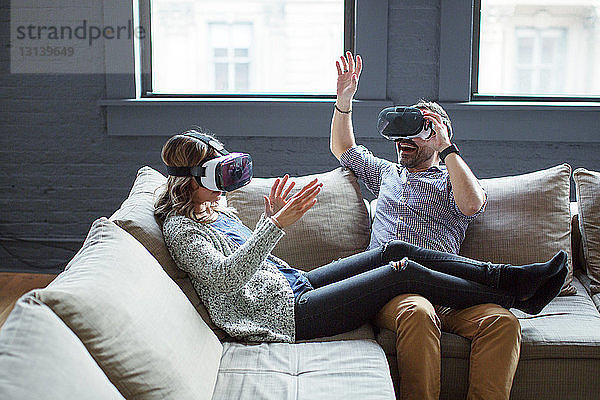 Kollegen tragen Virtual-Reality-Simulatoren  während sie im Büro auf dem Sofa sitzen