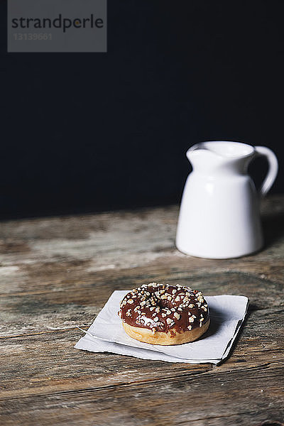 Schokoladendonut mit Wachspapier und Getränk auf Holztisch vor schwarzem Hintergrund