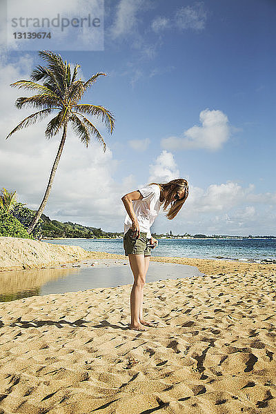 Frau zieht Hotpants am Strand gegen den Himmel aus