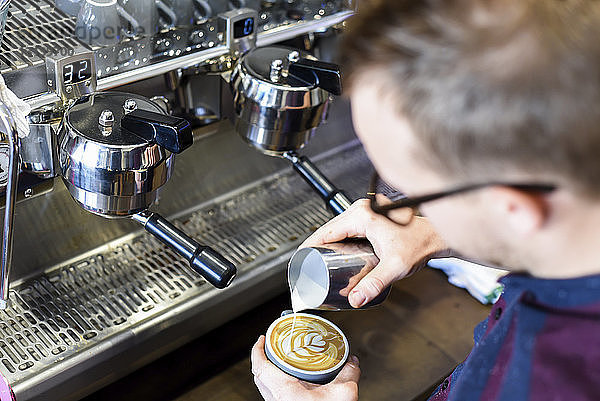 Barista gießt Milch in Kaffee  während er im Café ein schaumiges Getränk zubereitet