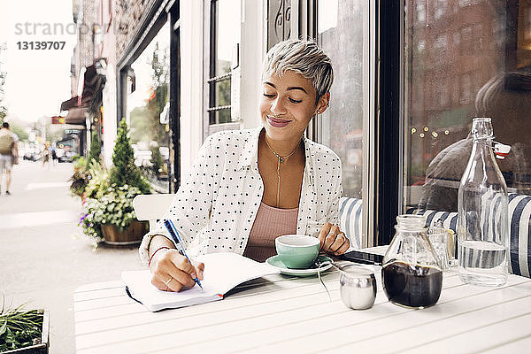 Glückliche Frau schreibt im Bürgersteig-Café in ihr Tagebuch