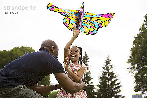 Niedrigwinkelansicht eines glücklichen Vaters und einer glücklichen Tochter  die mit einem Drachen gegen den Himmel spielen