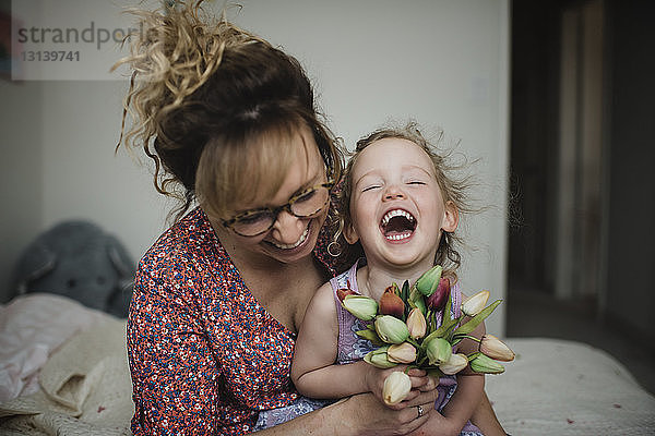 Glückliche Mutter mit Tochter  die Tulpen hält  während sie zu Hause auf dem Bett sitzt