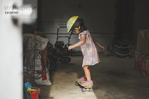 Seitenansicht eines Mädchens mit Helm  das in der Garage auf einem Skateboard steht
