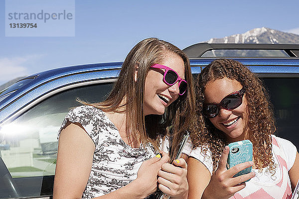 Freunde benutzen Mobiltelefon  während sie sich an ein Auto lehnen