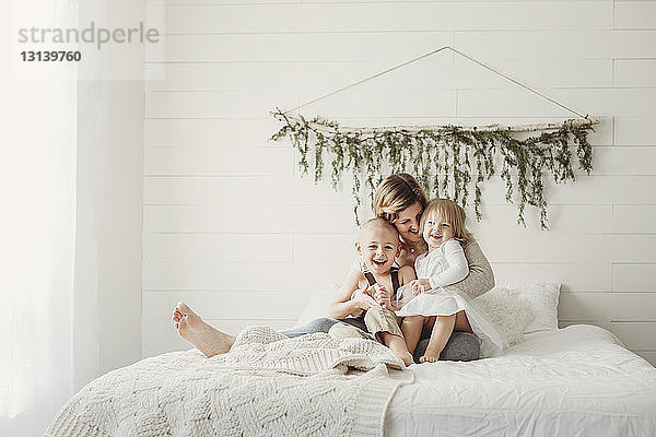 Glückliche Mutter mit Kindern zu Hause im Bett sitzend