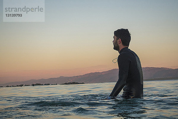 Seitenansicht eines männlichen Surfer im Meer vor klarem Himmel bei Sonnenuntergang