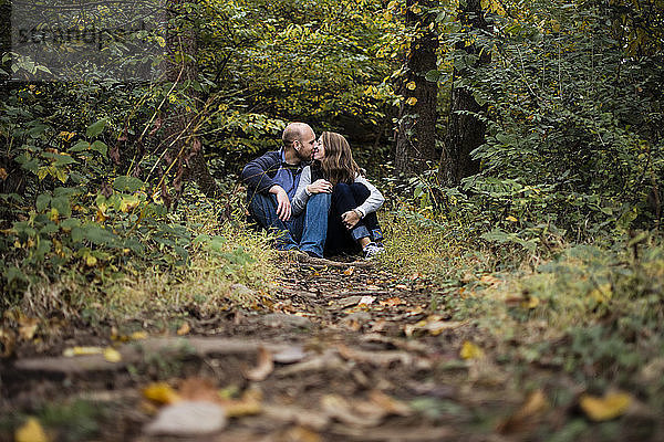 Paar küsst sich auf einem Feld im Wald sitzend