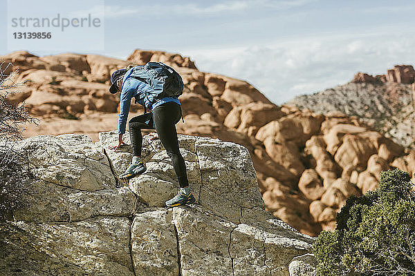 Wanderin mit Rucksack klettert bei Sonnenschein an Felsen