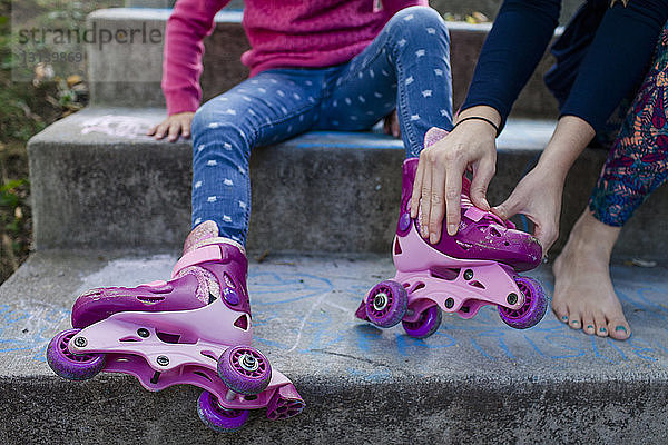 Niedriger Teil der Mutter hilft der Tochter beim Tragen von Rollschuhen beim Sitzen auf Stufen