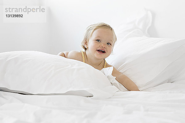 Porträt eines glücklichen kleinen Mädchens  das zu Hause auf dem Bett liegt