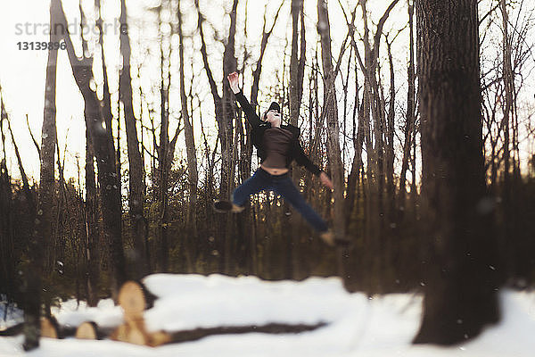 Teenager springt im Winter im Wald in voller Länge gegen Baumstämme