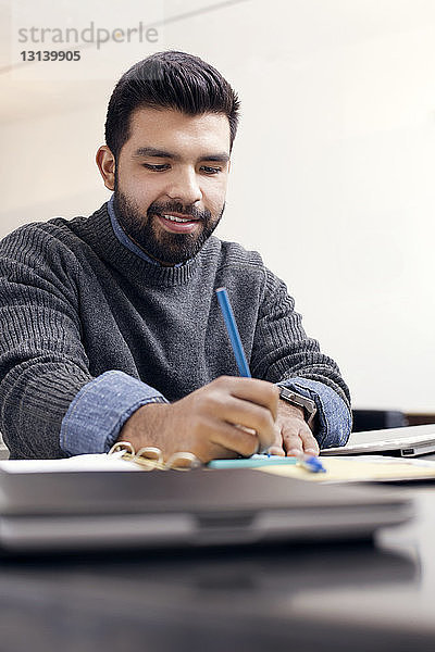 Lächelnder Geschäftsmann schreibt im Büro Tagebuch