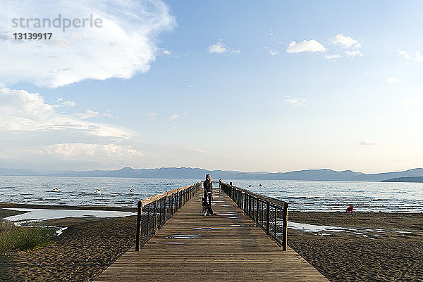 Frau mit Hund steht am Pier gegen den Himmel