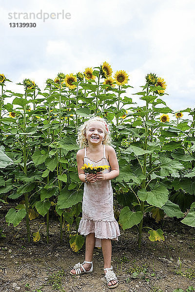 Fröhliches Mädchen hält Sonnenblumen  während es an Pflanzen steht