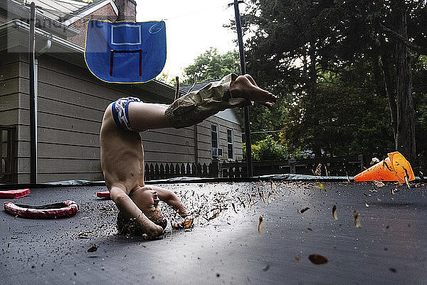 Junge ohne Hemd macht Kopfstand auf dem Trampolin im Hof