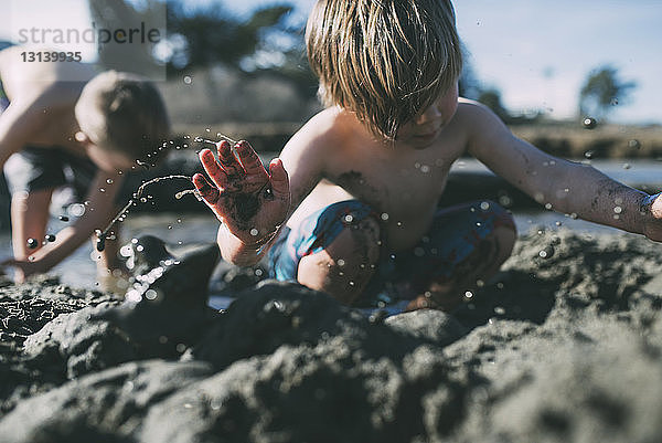 Brüder spielen am Strand im Schlamm