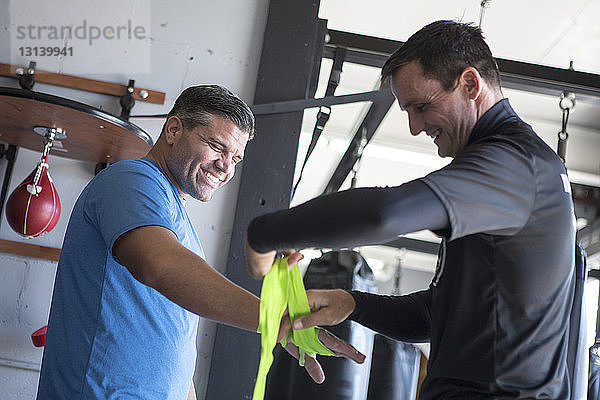 Niedrigwinkel-Ansicht eines Trainers  der die Hand eines männlichen Athleten mit Armband im Fitnessstudio umwickelt
