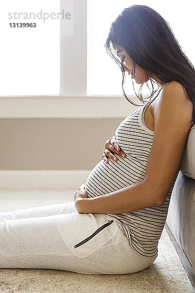 Seitenansicht einer lächelnden schwangeren Frau  die zu Hause am Sofa sitzt