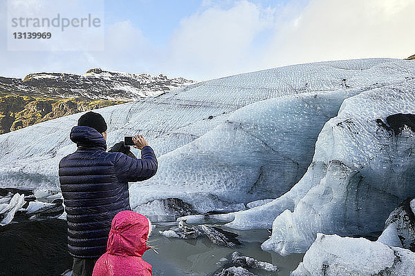 Rückansicht eines Vaters mit Tochter  der Gletscher fotografiert  während er gegen den Himmel steht