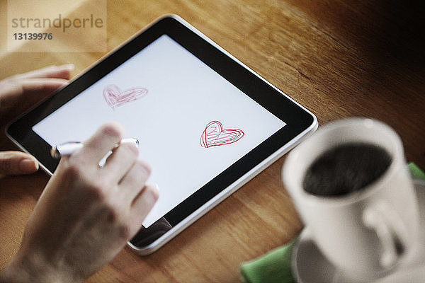 Ausgeschnittene Hände zeichnen im digitalen Tablett mit dem Stift auf dem Tisch