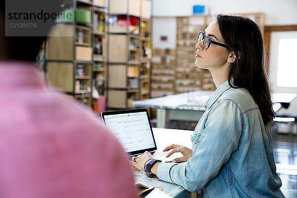 Geschäftsfrau schaut weg  während ein männlicher Kollege einen Laptop benutzt