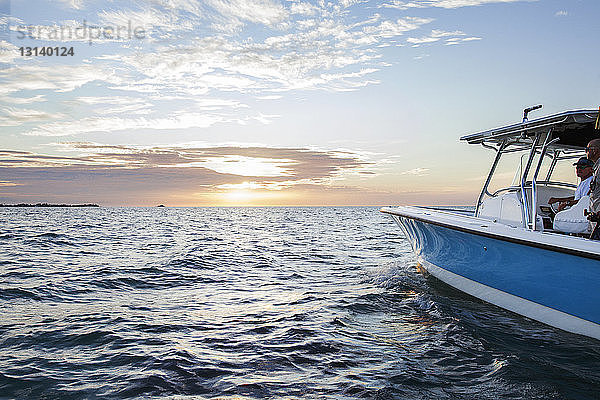 Männer  die bei Sonnenuntergang auf einem Boot auf See gegen den Himmel fahren