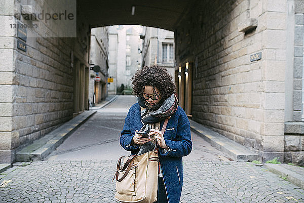Frau benutzt Smartphone  während sie auf einem gepflasterten Fußweg in der Stadt steht