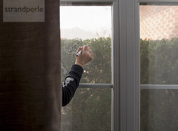 Geschnittene Hand eines Mädchens  das zu Hause mit Buntstift am Fenster zeichnet