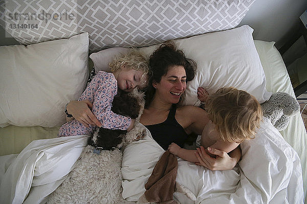 Hochwinkelansicht einer glücklichen Mutter mit Töchtern  die sich zu Hause im Bett entspannen