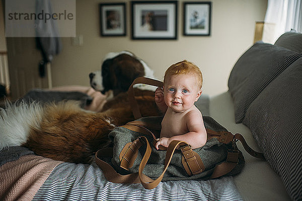 Porträt eines süßen kleinen Jungen in Umhängetasche sitzend mit Hund auf dem Bett