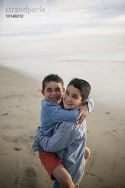 Porträt eines Jungen  der einen glücklichen Bruder trägt  während er am Strand steht