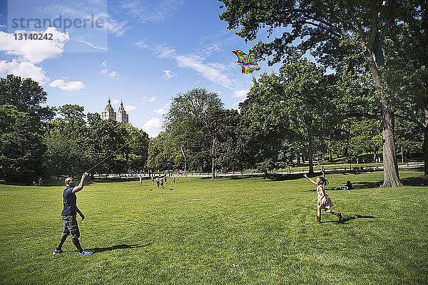 Vater und Mädchen spielen mit einem Drachen auf einem Grasfeld im Park
